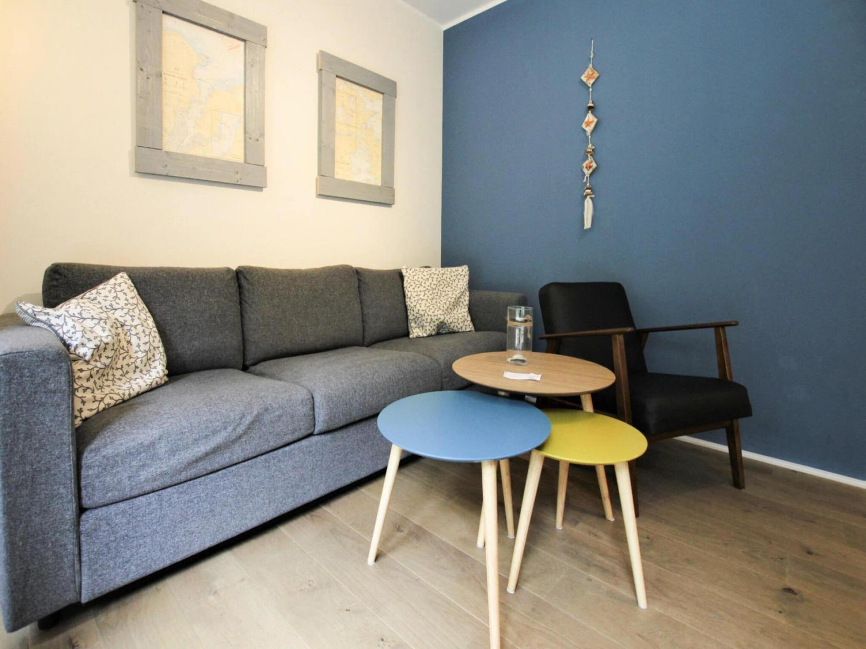 Ein modernes Wohnzimmer mit einem grauen Sofa, zwei kleinen runden Tischen, einem schwarzen Sessel und einer blauen Akzentwand.