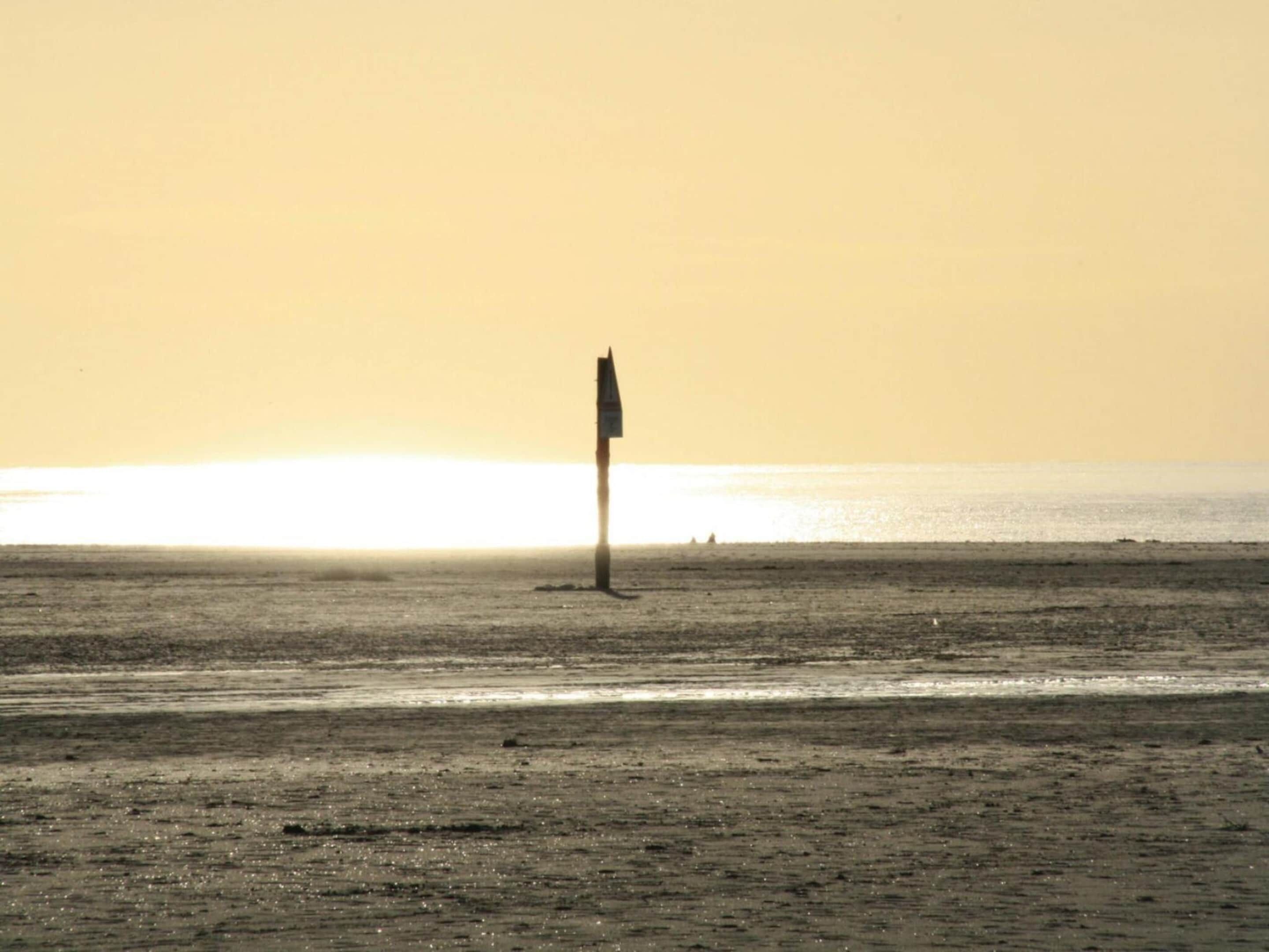 Een strand met een vlaggenmast in het midden, een heldere lucht en de oceaan op de achtergrond.