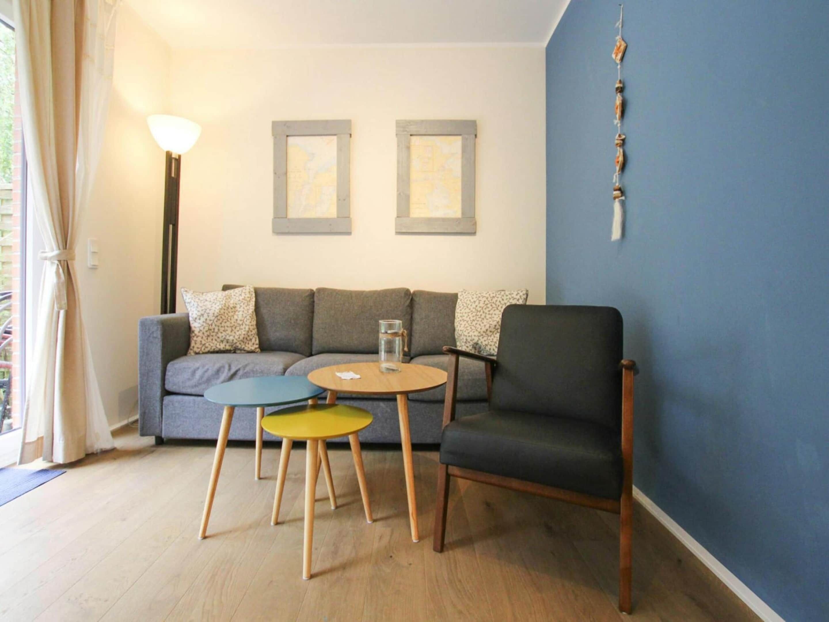 A living room with a sofa, two chairs, a coffee table, and a lamp. There are two framed pictures on the wall.