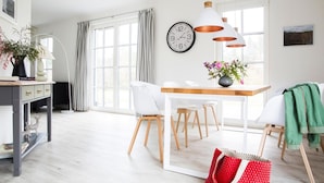 Ein helles, modernes Wohnzimmer mit Essbereich, großen Fenstern und einer Uhr an der Wand.