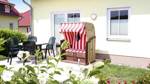 A patio with outdoor furniture, a wicker chair with a striped cover, and a white building with red roofs. - Doppelhaushalfte, Kuhlungsborn (Kuehlungsborn)