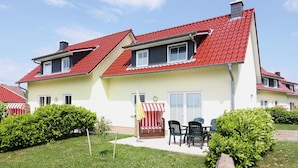A two-story house with a red-tiled roof, a small balcony, and a patio area with outdoor seating. - Doppelhaushalfte, Kuhlungsborn (Kuehlungsborn)