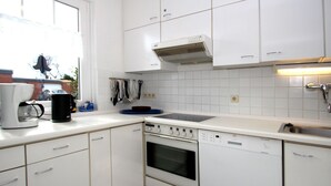 Een moderne keuken met witte kasten, een inbouwoven, een vaatwasser en een raam dat voor natuurlijk licht zorgt.
