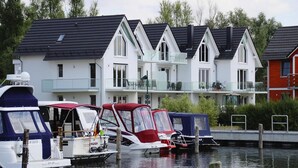 A marina with several boats docked. In the background, there are multi-story buildings with balconies. - Appartement Hafenflair am Plauer See (Plau am See)