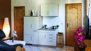 A compact kitchen with white cabinets, a wooden door, and a dining area with a table set for two. - Reihenhaus am Kummerower See, Sommersdorf (Sommersdorf)