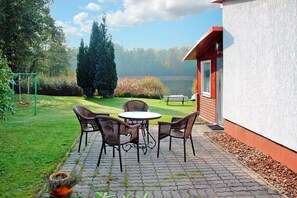 Un patio con sillas de mimbre y una mesa, un columpio y vistas a un lago y árboles.