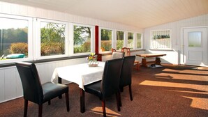 Ein Essbereich mit Tisch für vier Personen, umgeben von Stühlen, großen Fenstern mit Blick auf Bäume und einer T ür mit Fenster.