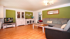Ein Wohnzimmer mit grauem Sofa, Couchtisch aus Holz und einem Fernseher auf einem Schrank.