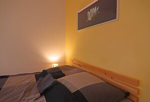 Ein Schlafzimmer mit zwei Betten, einem hölzernen Kopfteil, einem an der Wand befestigten Bild eines Lotusblüten und einer Nachttischlampe.