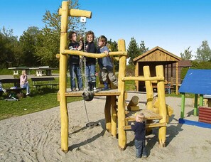 A playground with a wooden climbing structure and a small building in the background. - Feriendorf Ofingen, Bad Durrheim (Bad Duerrheim)