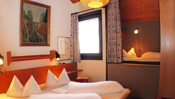 A hotel room with a bed, a nightstand, a lamp, a window with curtains, and a painting on the wall. - Feriendorf Ofingen, Bad Durrheim (Bad Duerrheim)