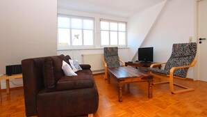 A living room with a brown leather sofa, two patterned armchairs, a wooden coffee table, and a TV on a stand. - Ferienwohnungen am Flacher See, Klocksin (Klocksin)