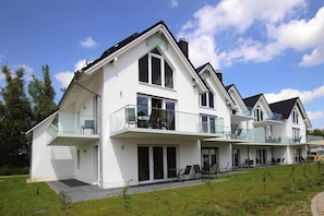 Une maison moderne à deux étages, dotée d’un balcon, de grandes fenêtres et d’une pelouse bien entretenue.