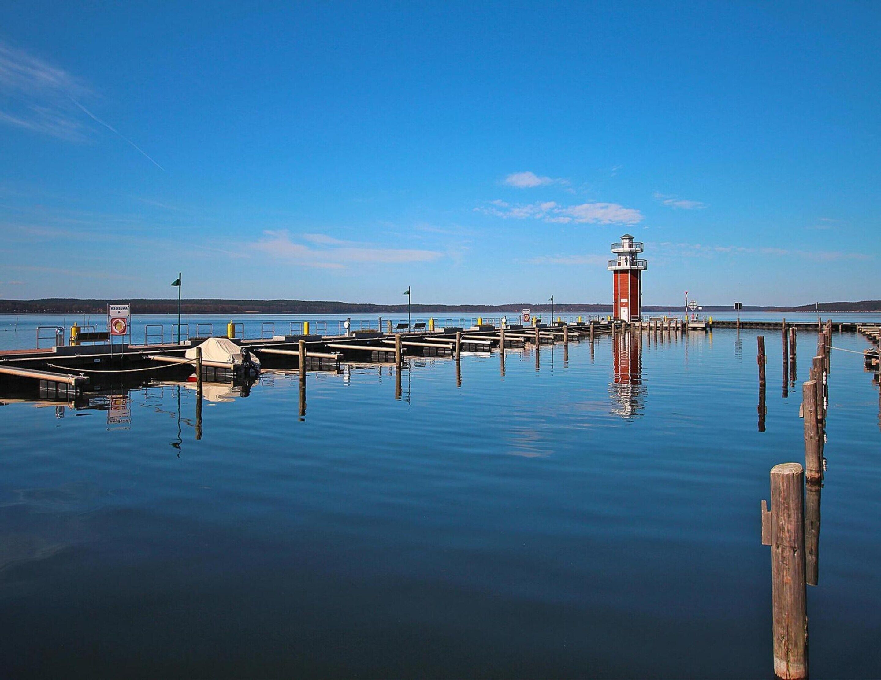 Un paysage paisible au bord de l’eau, avec un phare rouge, des quais en bois et un ciel bleu azur.