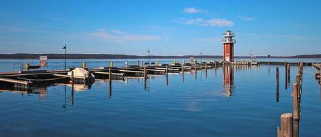 A calm waterfront with a red lighthouse, wooden docks, and a clear blue sky.