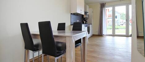 A dining area with a wooden table and four black chairs, a kitchenette with cabinets and appliances, and a sliding glass door leading to a balcony.