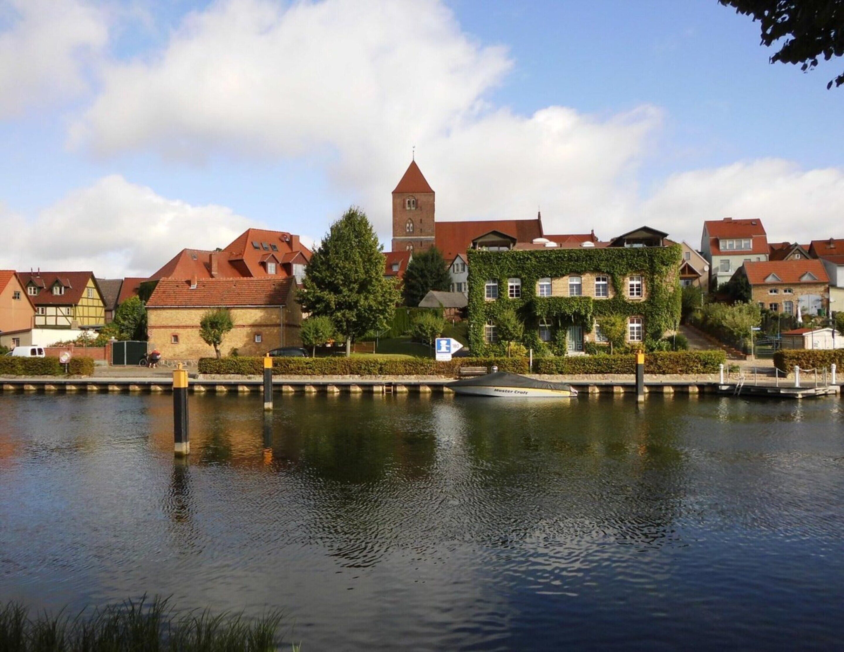 Un pueblo a orillas del río con edificios históricos, una torre y un embarcadero.