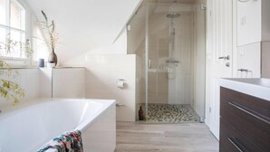 A modern bathroom with a bathtub, shower, and a glass-enclosed shower area. - Ferienhaus, Fuhlendorf (Fuhlendorf)