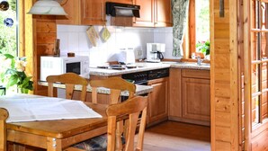 A wooden kitchen with a dining table, chairs, a microwave, a coffee maker, and a window with a view of greenery. - Familienfreundliches Ferienhaus mit Wlan in Hasselfelde (Oberharz am Brocken)