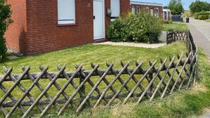 A brick building with a white door, numbered 13, and a small garden area with a wooden fence. - Bungalow Klonsnack in Dornumersiel (Dornum)