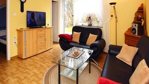 Olohuoneessa on sohva, lasinen sohvapöytä, televisio ja puinen kaappi.