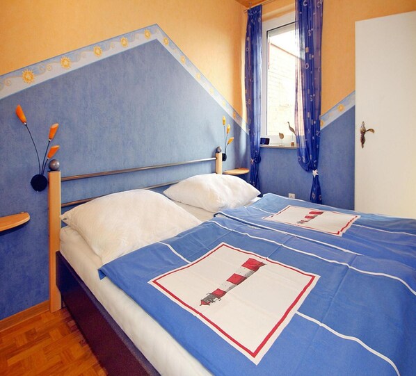 Une chambre à coucher avec un lit, deux oreillers, une tête de lit en bois, une fenêtre avec des rideaux et une porte.