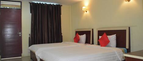 A hotel room with a large bed, two bedside tables, a wooden door, and curtains.