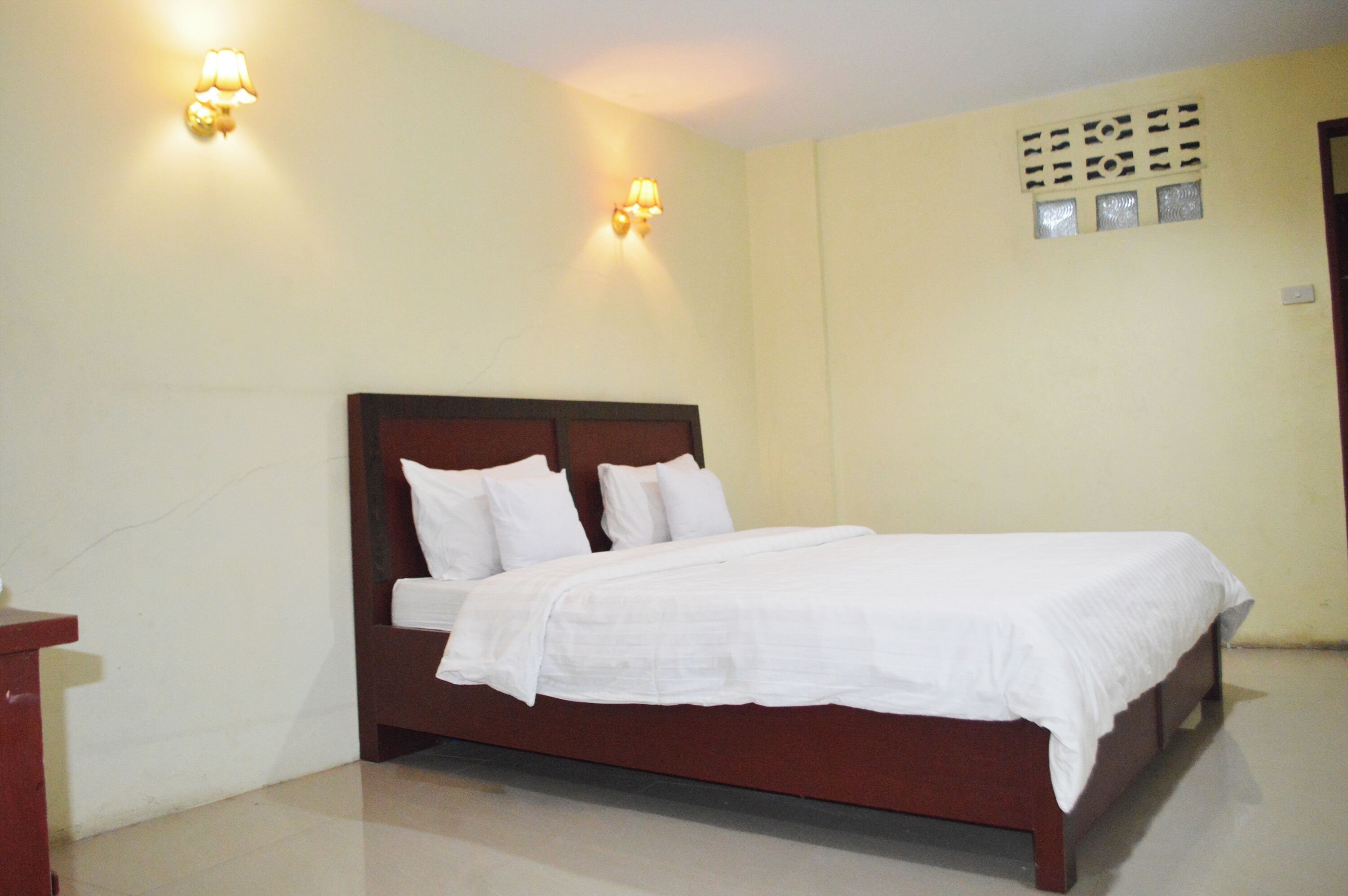 A bedroom with a wooden bed, white bedding, and two wall-mounted light fixtures.