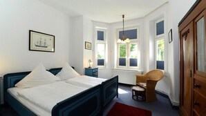 A bedroom with a large bed, a nightstand, a wicker chair, and a wardrobe. - Appartements, Wyk auf Fohr (Wyk auf Foehr)