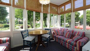 A sunroom with a dining table and chairs, a colorful sofa, and large windows with blinds. - Appartements, Wyk auf Fohr (Wyk auf Foehr)