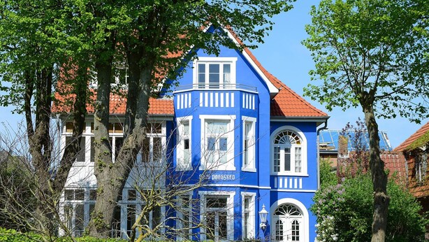 A blue building with a red roof, surrounded by trees and greenery. - Appartements, Wyk auf Fohr (Wyk auf Foehr)