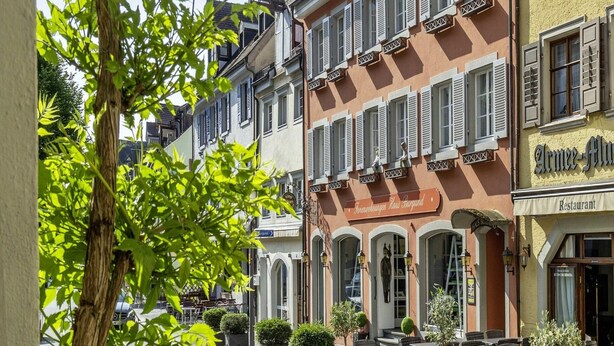 Eine Straße mit traditioneller europäischer Architektur, darunter ein Restaurant namens "Armée-Gloucester" und ein Gebäude mit der Aufschrift "Fleurettchen Haus Burgund".