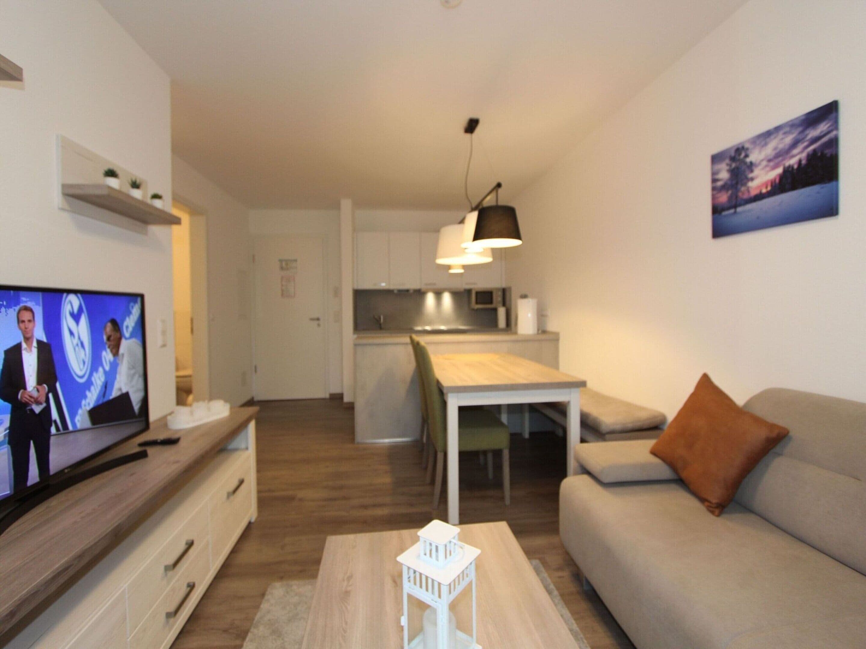 A modern living room with a television, a sofa, a coffee table, and a kitchen in the background.