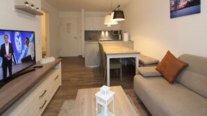 Un salon moderne avec une télévision, un canapé, une table basse et une cuisine en arrière-plan.