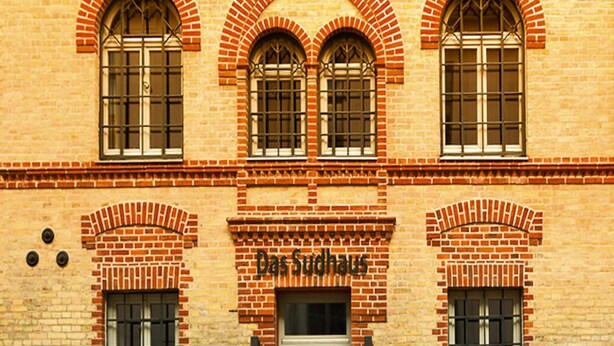Un bâtiment doté de trois fenêtres en arc de cercle et d’une porte, portant l’inscription « Das Sudhaus ».