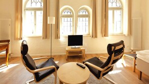 Un salon moderne avec deux fauteuils en cuir, une table ronde en bois, un téléviseur à écran plat et un piano.