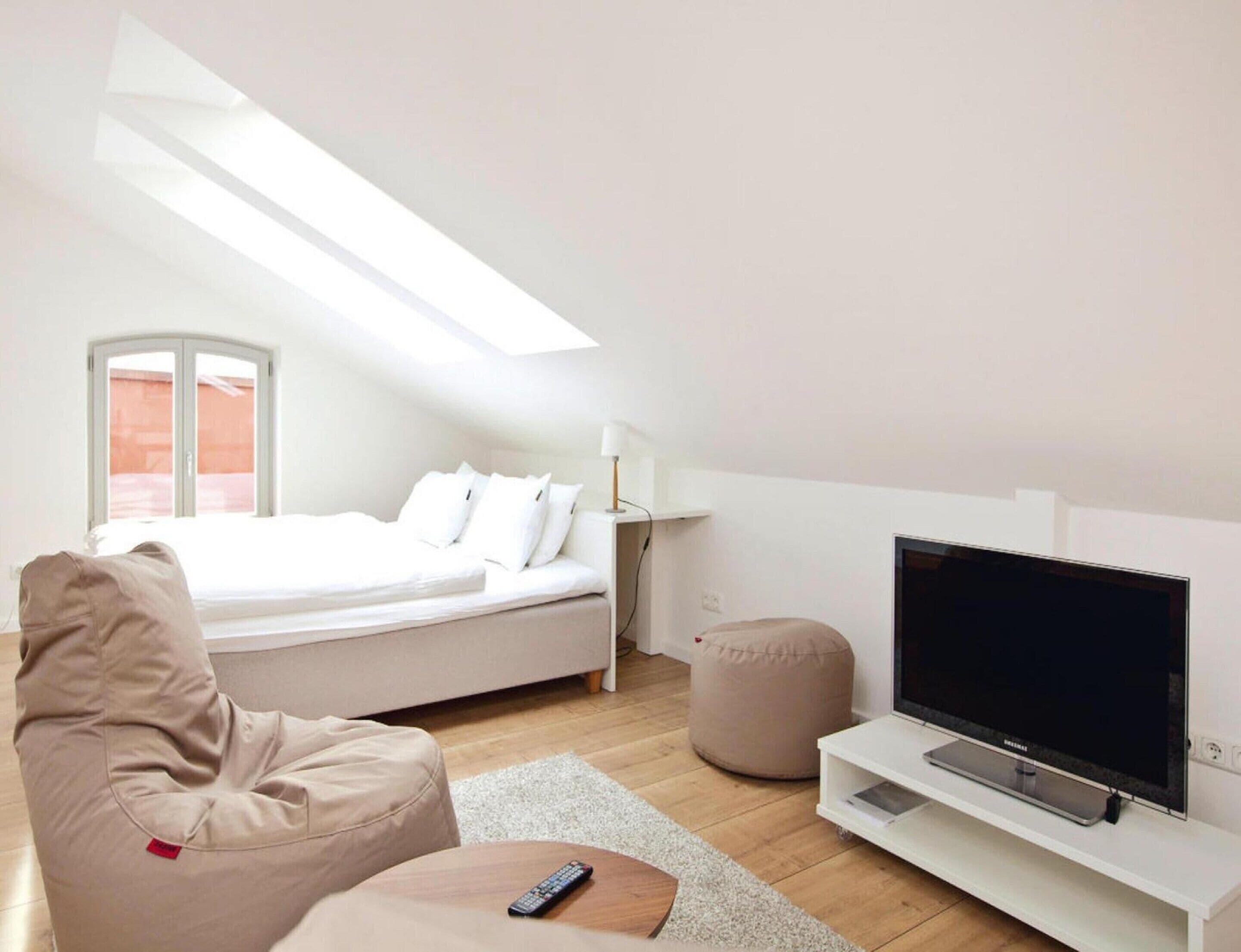 A modern bedroom with a bed, a TV, a bean bag chair, and a skylight.