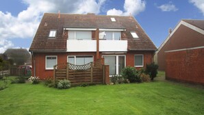 Ein zweistöckiges Haus mit flachem Dach, einem Vorgarten und einem Holztor.