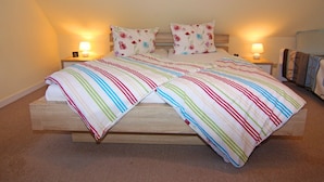 A bed with a striped bedspread and two pillows, two bedside lamps, and a wooden headboard. - Wohnung in Zinnowitz Nahe Meeresstrand (Zinnowitz)