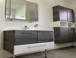 A modern bathroom with a white vanity, dark wood cabinets, and a glass shelf above the sink. - Ferienwohnung in Mirow for 4 Personen (Mirow)