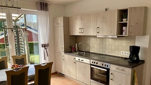 A modern kitchen with light wood cabinets, a stainless steel stove, and a dining area with a table and chairs.