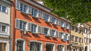 Un immeuble à la façade rouge, doté de nombreuses fenêtres avec volets et d’une enseigne indiquant « Fernewohnungen Haus Burgund ».