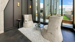 Ein modernes Interieur mit zwei Sesseln, einem kleinen runden Tisch und einem großen Fenster mit Blick auf ein Gebäude und Grünflächen.