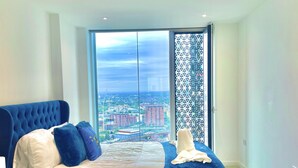 Ein Schlafzimmer mit einem großen Bett, Blick auf die Stadt und einem Balkon mit einem gemusterten Geländer.