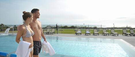 Ein Paar steht an einem Pool mit Liegestühlen und einem Rasen im Hintergrund.