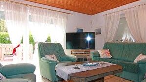 A living room with a television, green sofas, a coffee table, and a wooden ceiling. - Ferienwohnung im Ferienhaus Rosi, Fehmarn-schlagsdorf (Fehmarn)