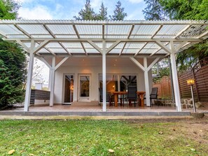 A covered patio with a stone wall, a wooden table, and chairs. - Ferienhaus mit Terrasse und Kaminofen in Parchim (Parchim)