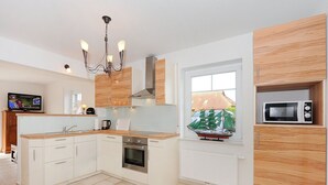 Une cuisine moderne avec des meubles blancs, un four encastré, un four à micro-ondes et une fenêtre donnant sur des maisons.