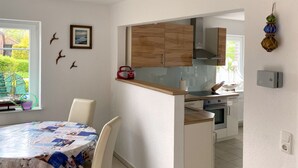 Une cuisine moderne avec des meubles blancs, un plan de travail en bois et un coin repas où une table est recouverte d’un journal.