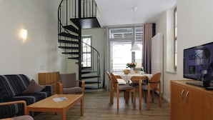 Un salon comprenant un canapé, des fauteuils, une table, un téléviseur, un escalier en colimaçon et une fenêtre donnant sur un beau paysage.
